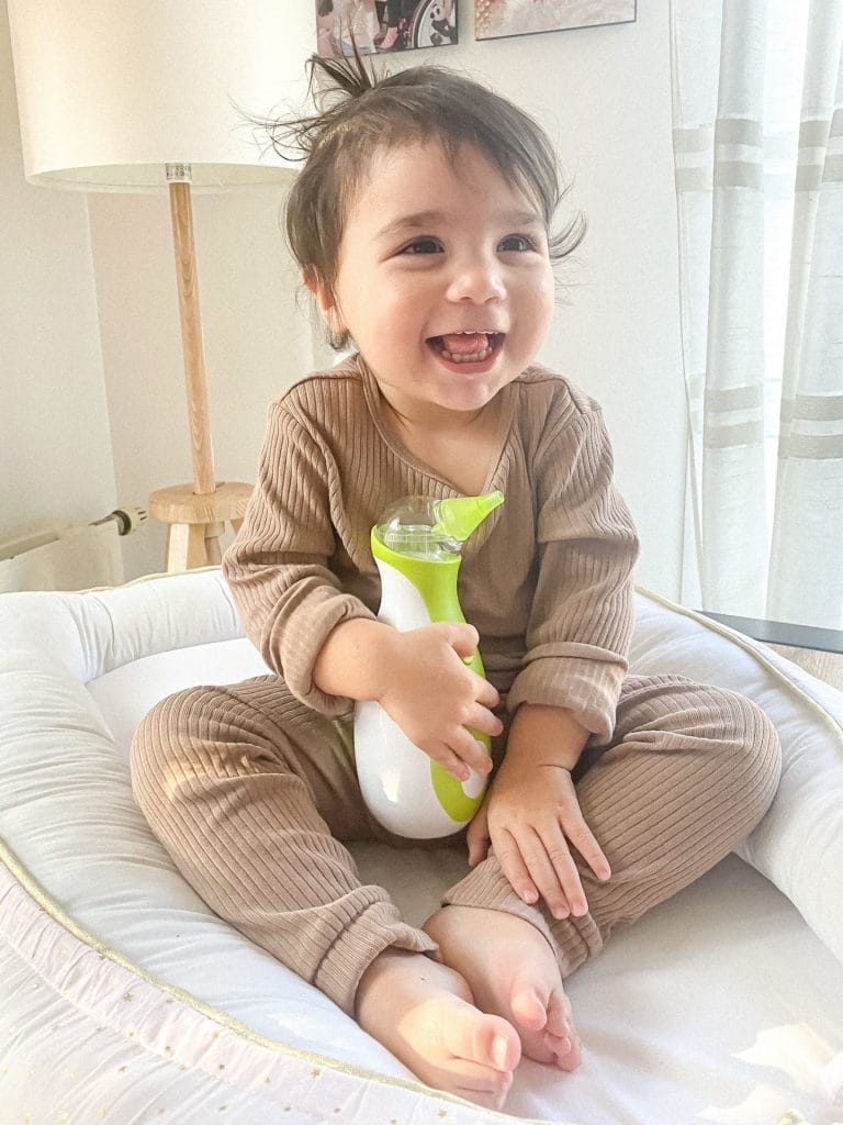 Lächelndes kleines Mädchen in einem Babynest mit einem tragbaren elektrischen Nasensauger Nosiboo Go