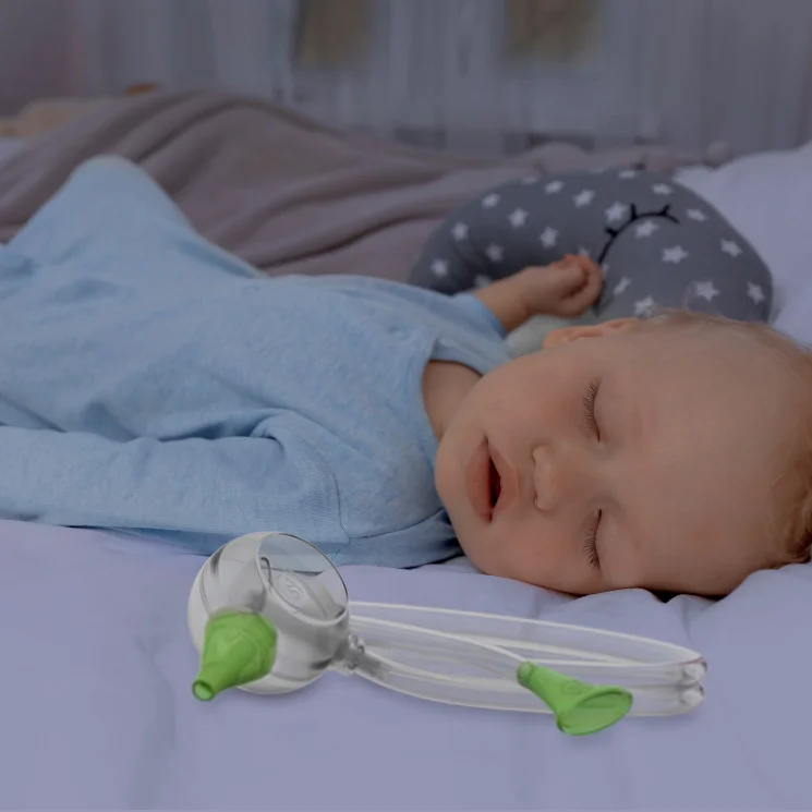 A baby boy sleeping peacefully in his bed next to the Nosiboo Eco Manual Nasal Aspirator