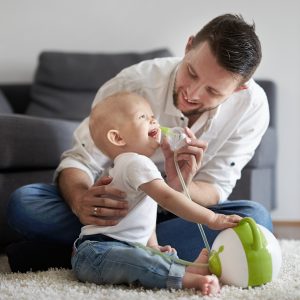 Öffnen Sie das Bild eines Vaters, der seinem Sohn mit Hilfe des elektrischen Baby Nasensaugers Nosiboo Pro die verstopfte Nase reinigt