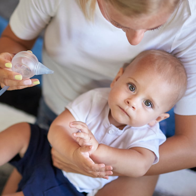 Eine Mutter hält auf ihrem Schoß ihren süßen, kleinen Jungen und putzt mit Hilfe des Nosiboo Pro elektrischen Baby Nasensaugers seine verstopfte Nase