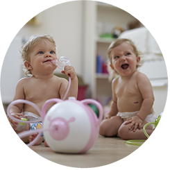 Zwei glückliche Babys sitzen auf dem Fußboden mit dem Nosiboo Pro elektrischen Baby Nasensauger