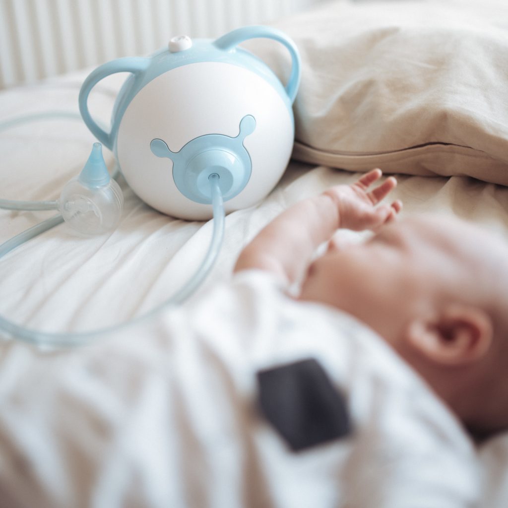 Sleeping baby next to a blue Nosiboo Pro electric nasal aspirator
