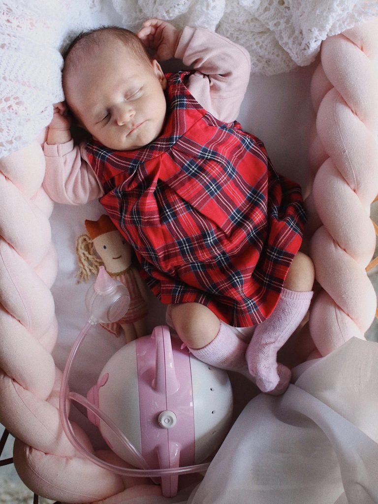 Une petite fille dormant paisiblement dans son lit, avec un mouche-bébé électrique Nosiboo Pro rose