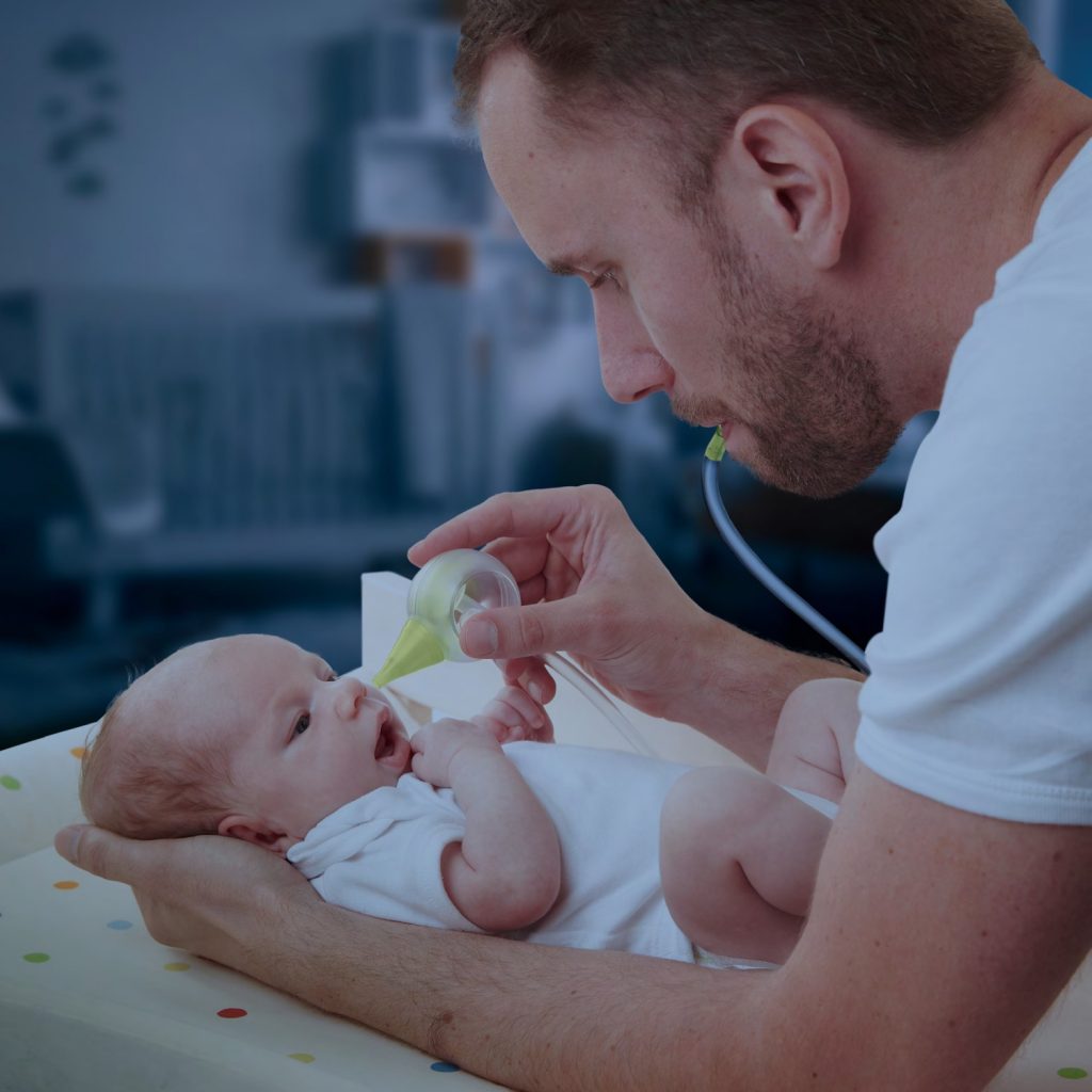 Ein Vater hält sein Neugeborenes und saugt seine Nase mit einem manuellen Nosiboo Eco Nasensauger ab