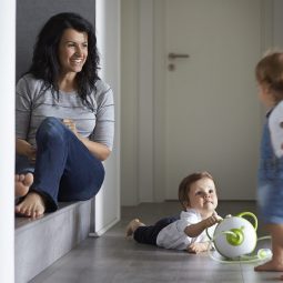 Öffnen Sie das Bild einer Mutter mit ihrem Sohn und ihrer Tochter, die mit dem Nosiboo Pro elektrischen Baby Nasensauger zu Hause auf dem Boden sitzen